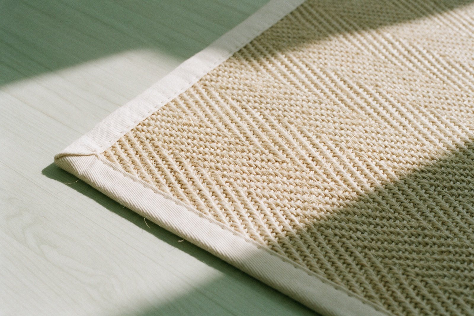 Detalhe de um tapete de sisal bege com trama grossa em espinha e acabamento de cadarço na borda, sobre piso de madeira Detalhe de um tapete de sisal bege com trama grossa em espinha e acabamento de cadarço na borda, sobre piso de madeira